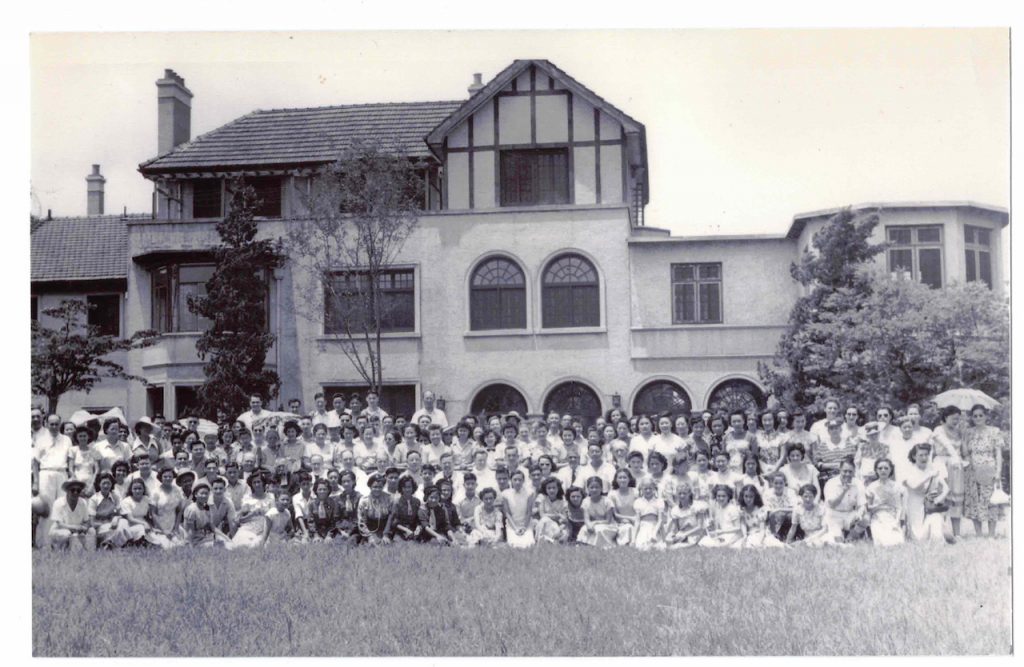 Archival photo of a large group of people posing for a photo in front of a building