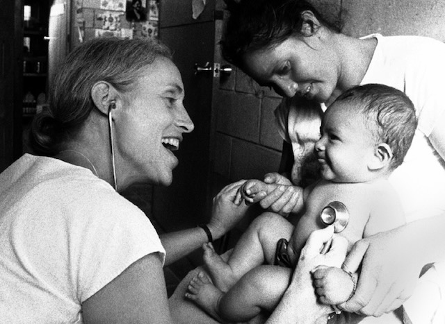 A doctor smiling and providing medical care to a happy baby held by another woman.