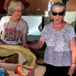 Three older women are pictured standing and talking as they volunteer with a food pantry in new Mexico.