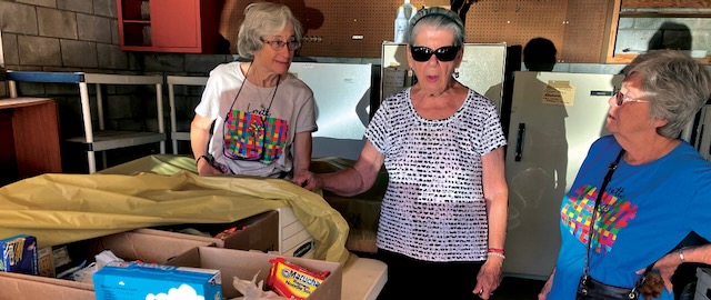 Three older women are pictured standing and talking as they volunteer with a food pantry in new Mexico.