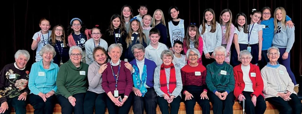 A large group picture of a wide variety of ages sitting and standing together for a group picture indoors. They are wearing name tags.