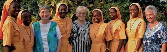 Young Ghanian sisters in orange habits take a group photo with three Sisters of Loretto in regular clothing.