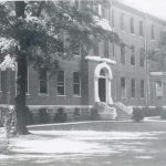 Black and white photo of a large building with stone steps leading up to a white framed door.