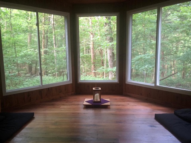 A view of a small chapel with a small looking out of huge clear windows into the green woods.