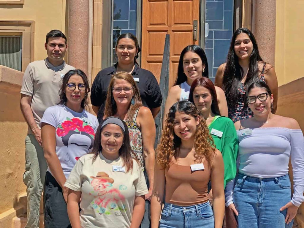 A group of Latino social work and law students stand staggered on three steps to take a group photo. There are nine women and one man.