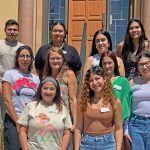 A group of Latino social work and law students stand staggered on three steps to take a group photo. There are nine women and one man.