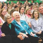 A photo of a school assembly with several Loretto members in the front row of chairs and rows of high school students behind them.