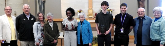 A group of ten people of various ages in a row smiling for a group photo as they celebrate two teens for winning a social justice award.