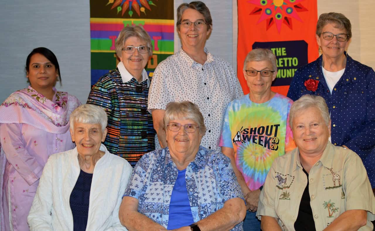 A happy group of women smiling together at a Loretto Community gathering, all wearing a variety of different colors and patterns.