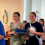 A white haired nun in a blue t-shirt leads a group of confirmation students down the aisle of a church.