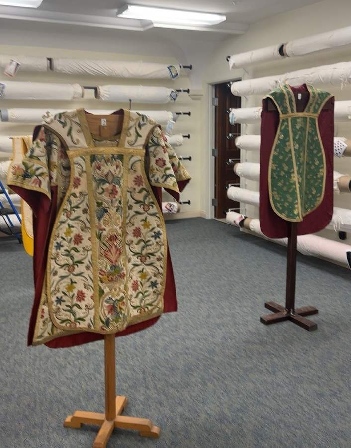 Two ornate vestments wait on display stands.