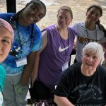 Two older Sisters with white hair take a photo with another adult and three students as they take a break from gardening.