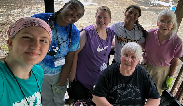 Two older Sisters with white hair take a photo with another adult and three students as they take a break from gardening.