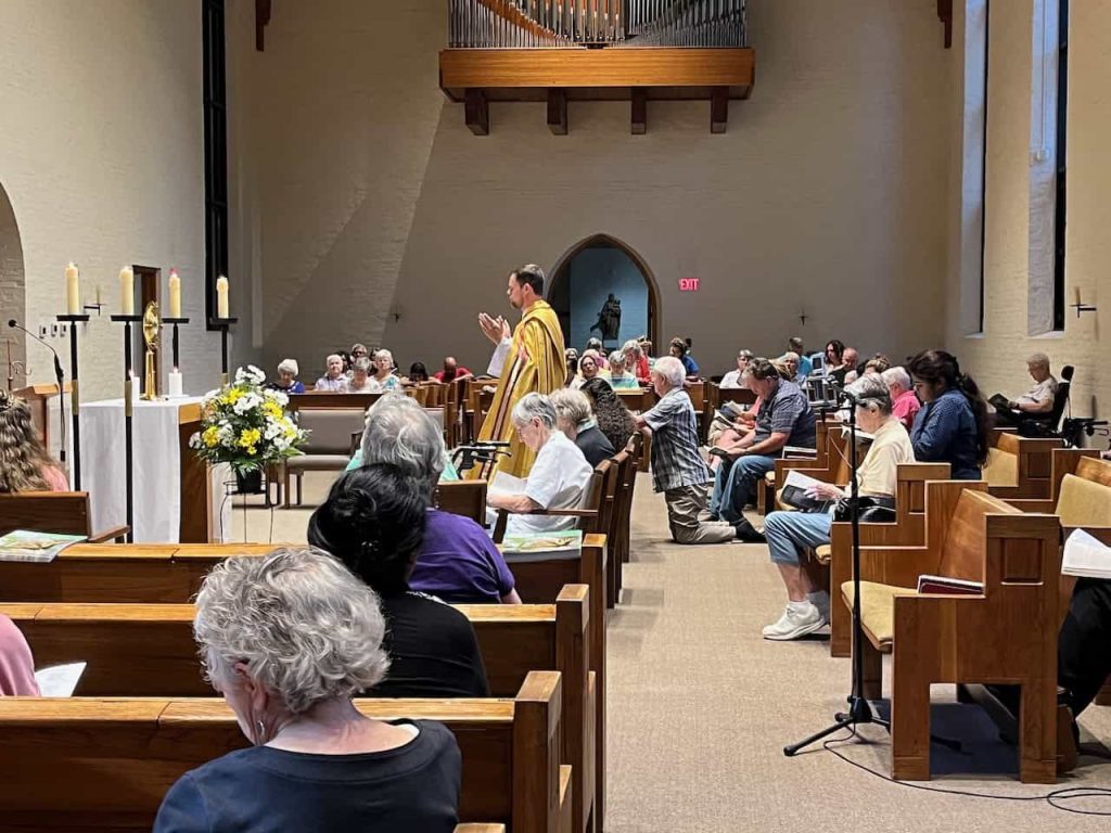 A priest has his arms open leading a crowded Mass in the Loretto Motherhouse chapel.