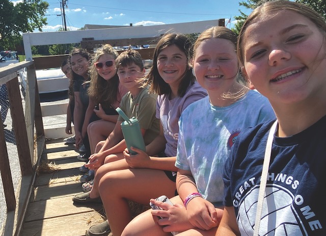 A group of seven confirmation students sitting on a hay wagon outside smiling as they are about to take a ride.