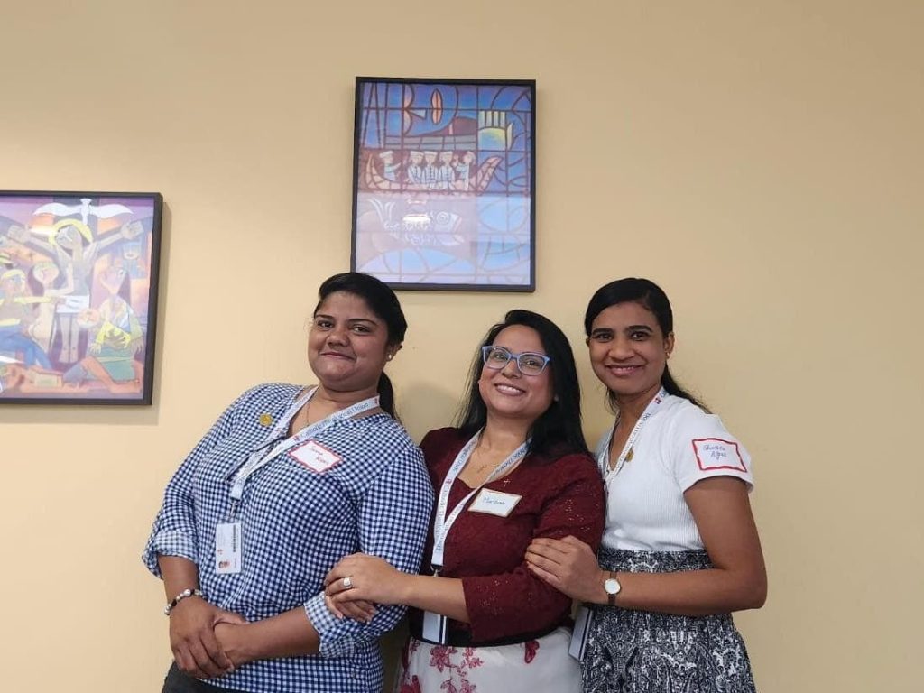 Three young Pakistani women in their 20s and 30s standing together smiling for a photo.